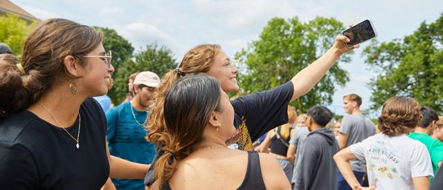 Group of friends taking a selfie outdoors at a social gathering.